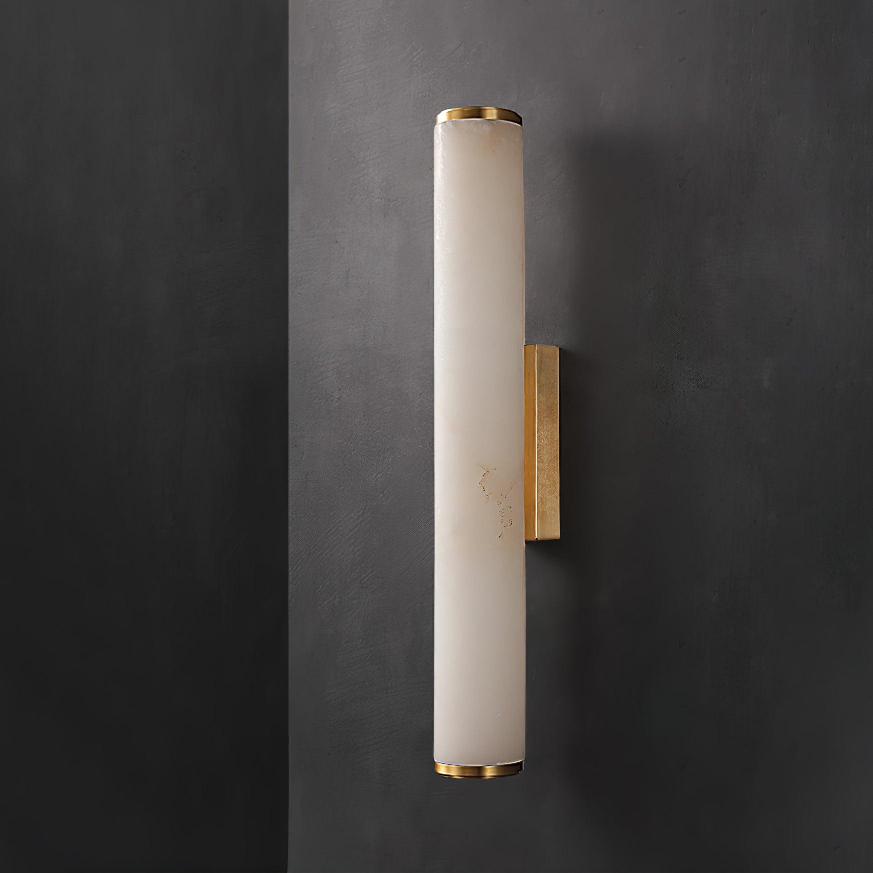 Wall lamp with a long pale veined stone-look tube and a gold-toned bracket, unlit, on a dark grey wall.