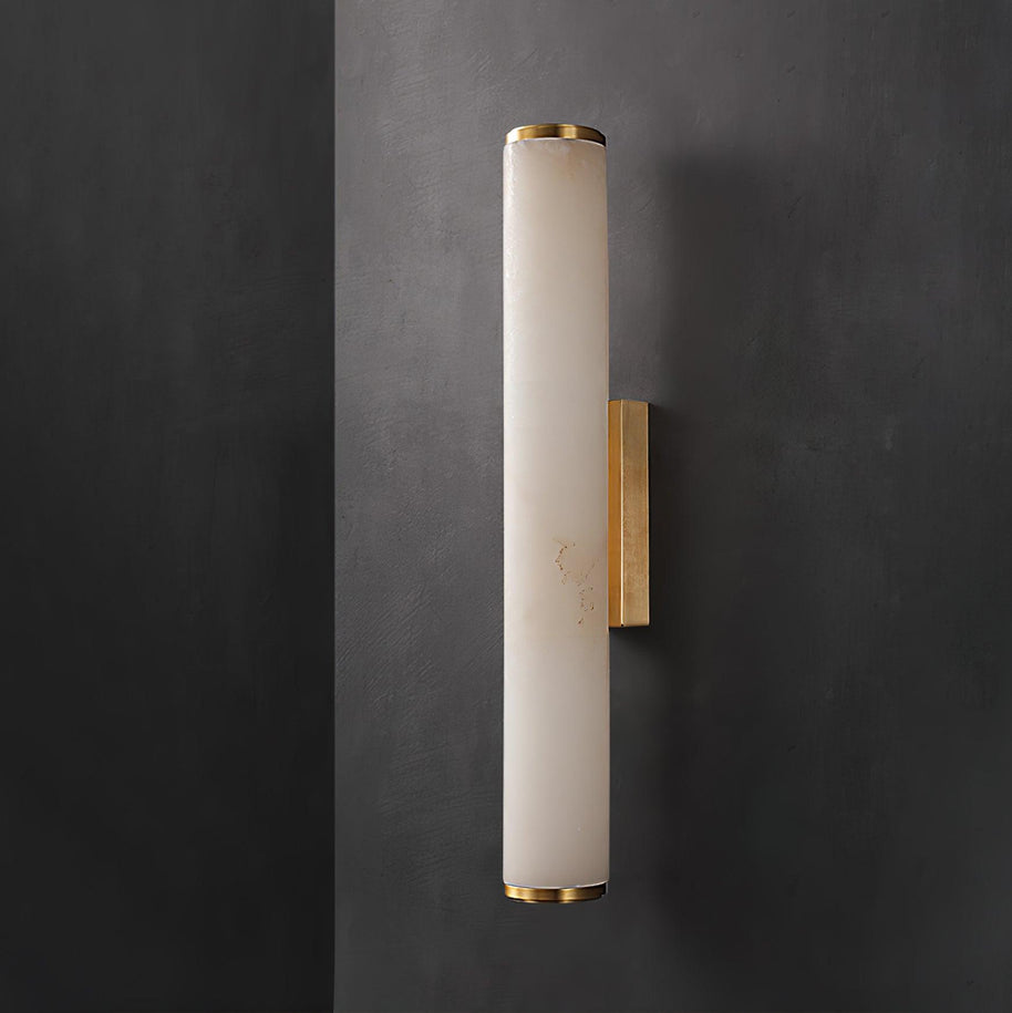 Wall lamp with a long pale veined stone-look tube and a gold-toned bracket, unlit, on a dark grey wall.
