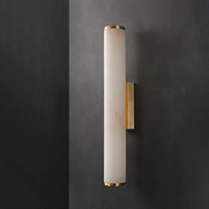 Wall lamp with a long pale veined stone-look tube and a gold-toned bracket, unlit, on a dark grey wall.