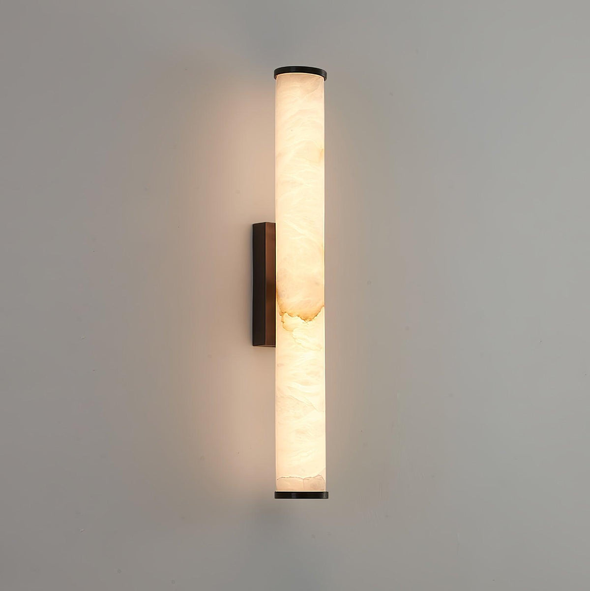 Wall lamp with a long pale veined stone-look tube and a dark bracket, lit, on a pale grey wall.