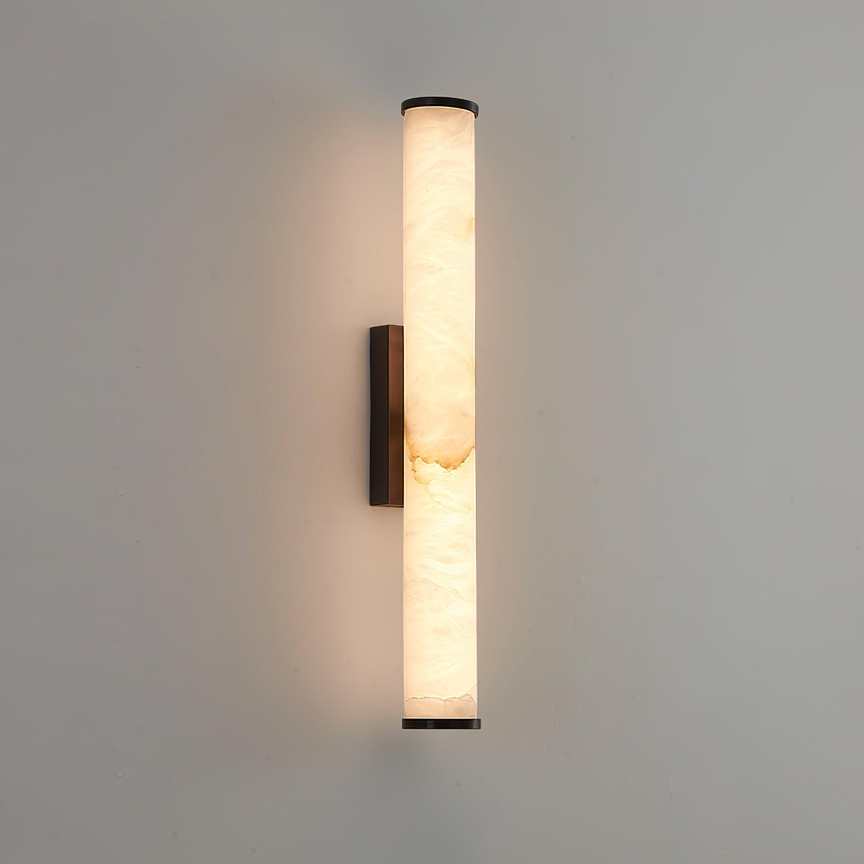 Wall lamp with a long pale veined stone-look tube and a dark bracket, lit, on a pale grey wall.