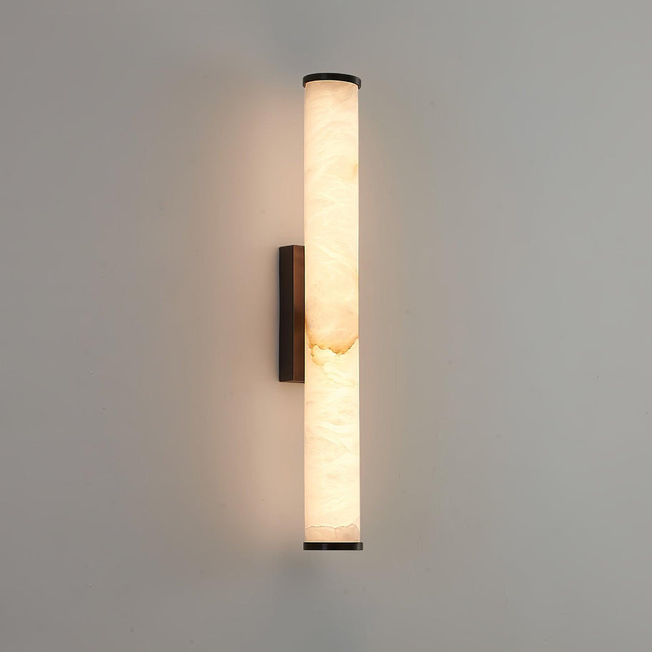 Wall lamp with a long pale veined stone-look tube and a dark bracket, lit, on a pale grey wall.