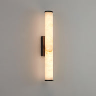 Wall lamp with a long pale veined stone-look tube and a dark bracket, lit, on a pale grey wall.