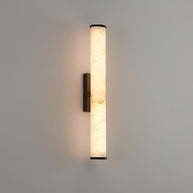 Wall lamp with a long pale veined stone-look tube and a dark bracket, lit, on a grey wall.