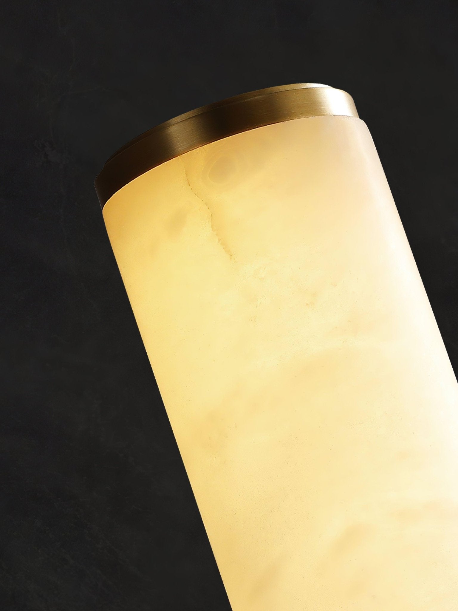 Close view of the brass-coloured end cap and the veined alabaster tube, lit.