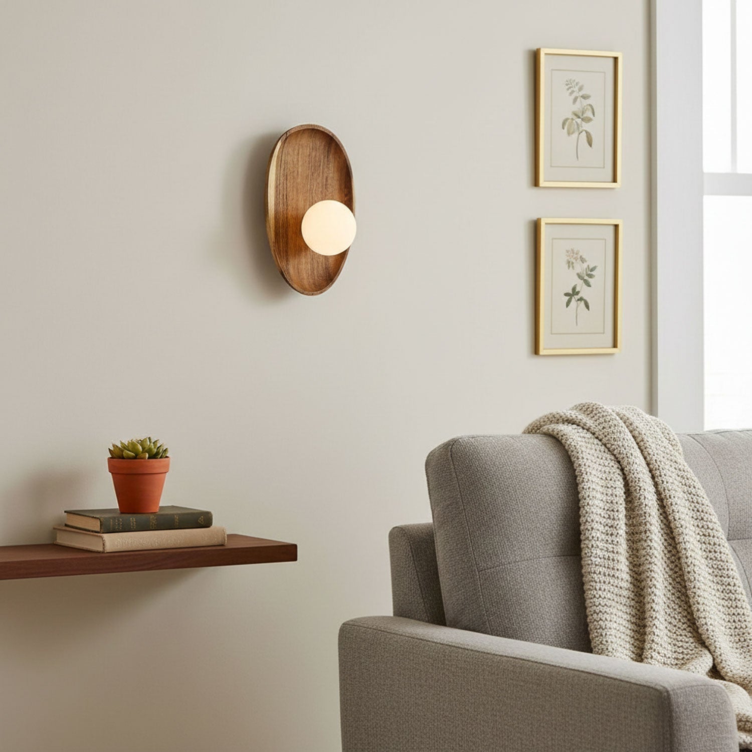 Wall lamp with a shaped walnut-coloured wooden backplate and a white glass globe on a wall beside two framed botanical prints.