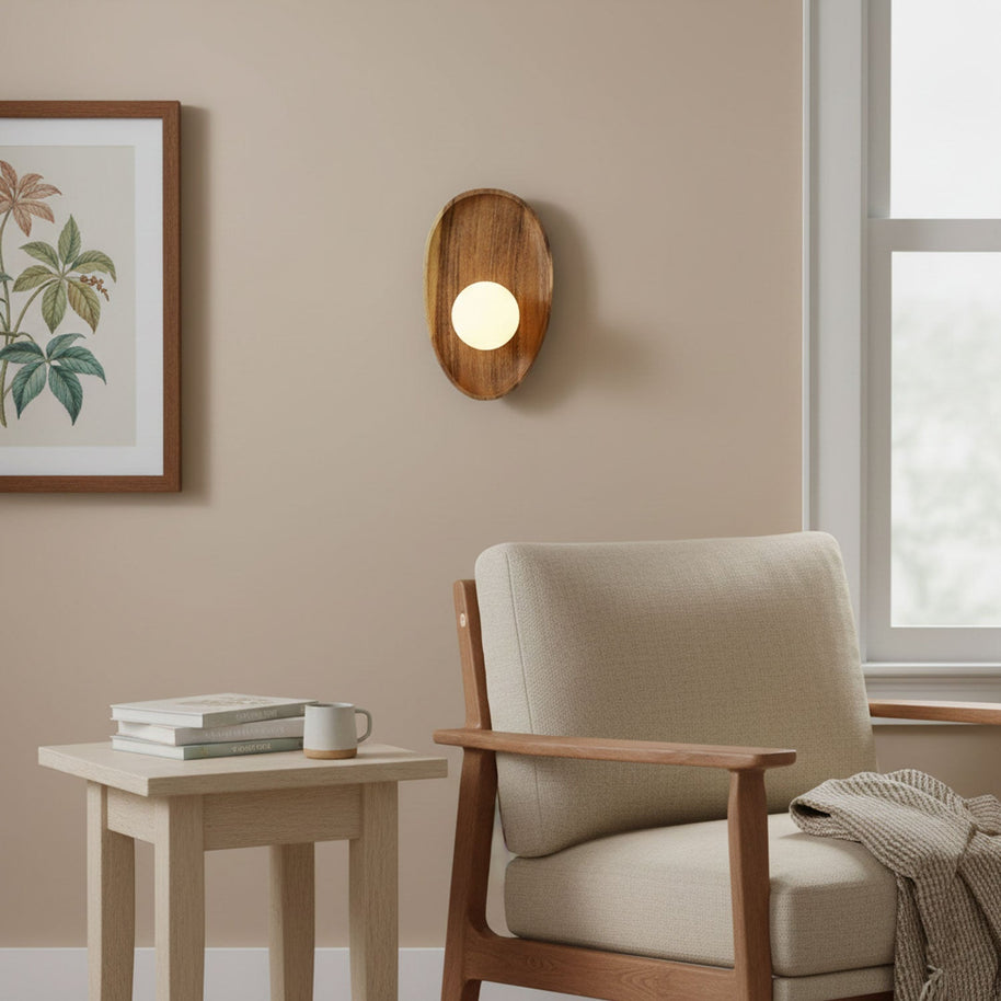 Wall lamp with a shaped walnut-coloured wooden backplate and a white glass globe lit on a wall beside a framed botanical print.