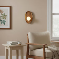 Wall lamp with a shaped walnut-coloured wooden backplate and a white glass globe lit on a wall beside a framed botanical print.