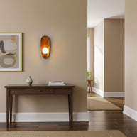 Wall lamp with a shaped walnut-coloured wooden backplate and a white glass globe lit above a console table in a hallway.
