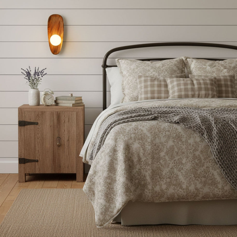 Wall lamp with a shaped walnut-coloured wooden backplate and a white glass globe lit on a white boarded wall above a bedside cabinet.