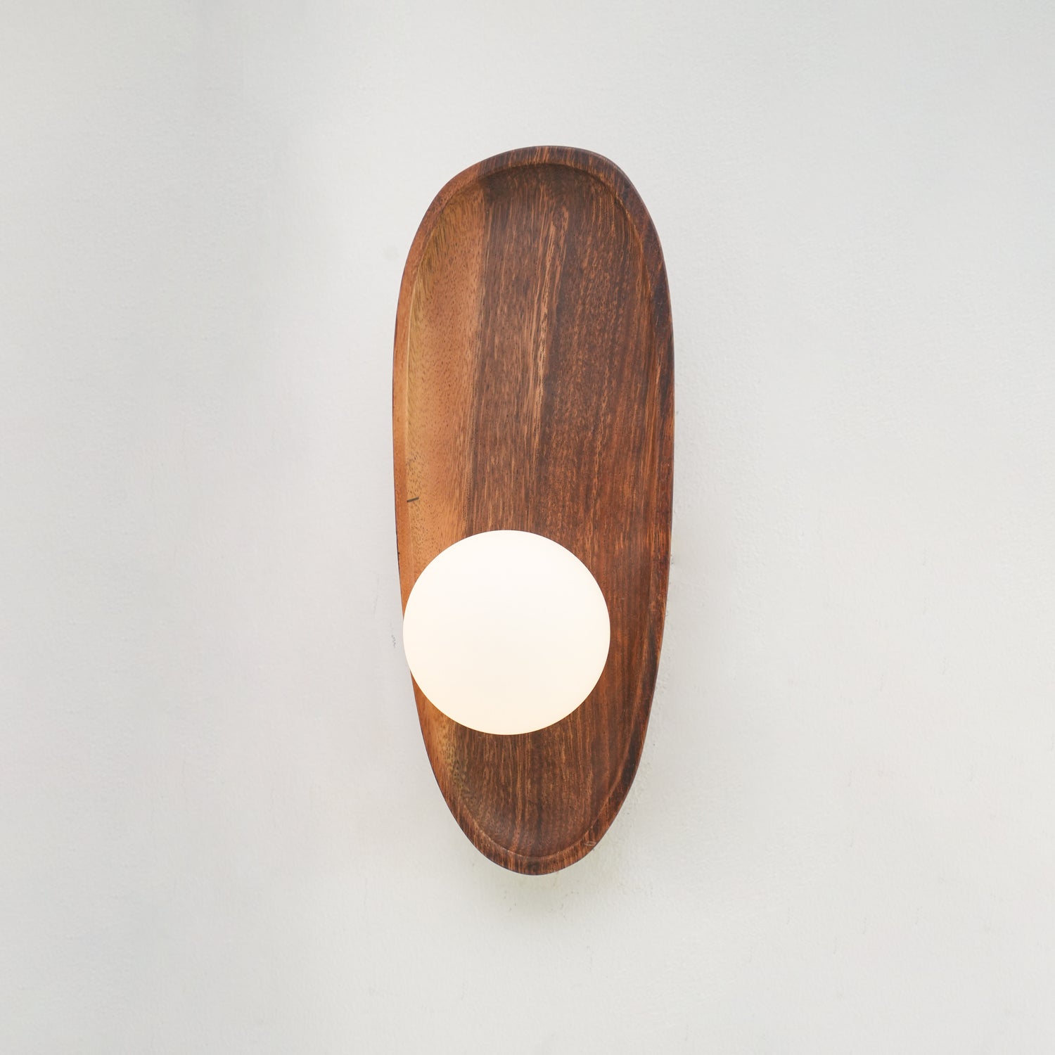 Wall lamp with a shaped walnut-coloured wooden backplate and a white glass globe, narrow upright shape, unlit on a plain wall.