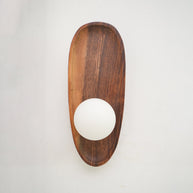 Wall lamp with a shaped walnut-coloured wooden backplate and a white glass globe lit, narrow upright shape, shown close on a plain wall.