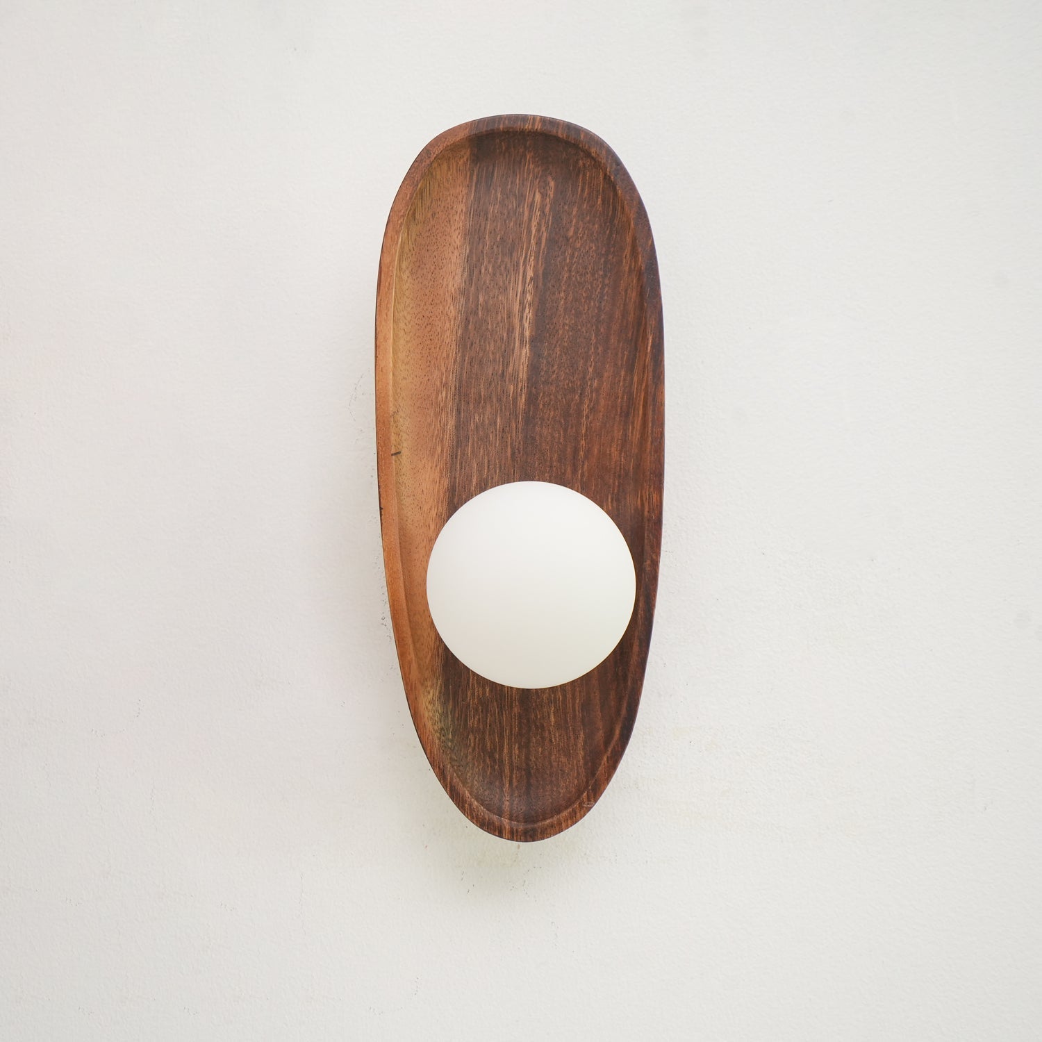 Wall lamp with a shaped walnut-coloured wooden backplate and a white glass globe, narrow upright shape, shown close and unlit.