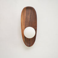 Wall lamp with a shaped walnut-coloured wooden backplate and a white glass globe, narrow upright shape, shown close and unlit.