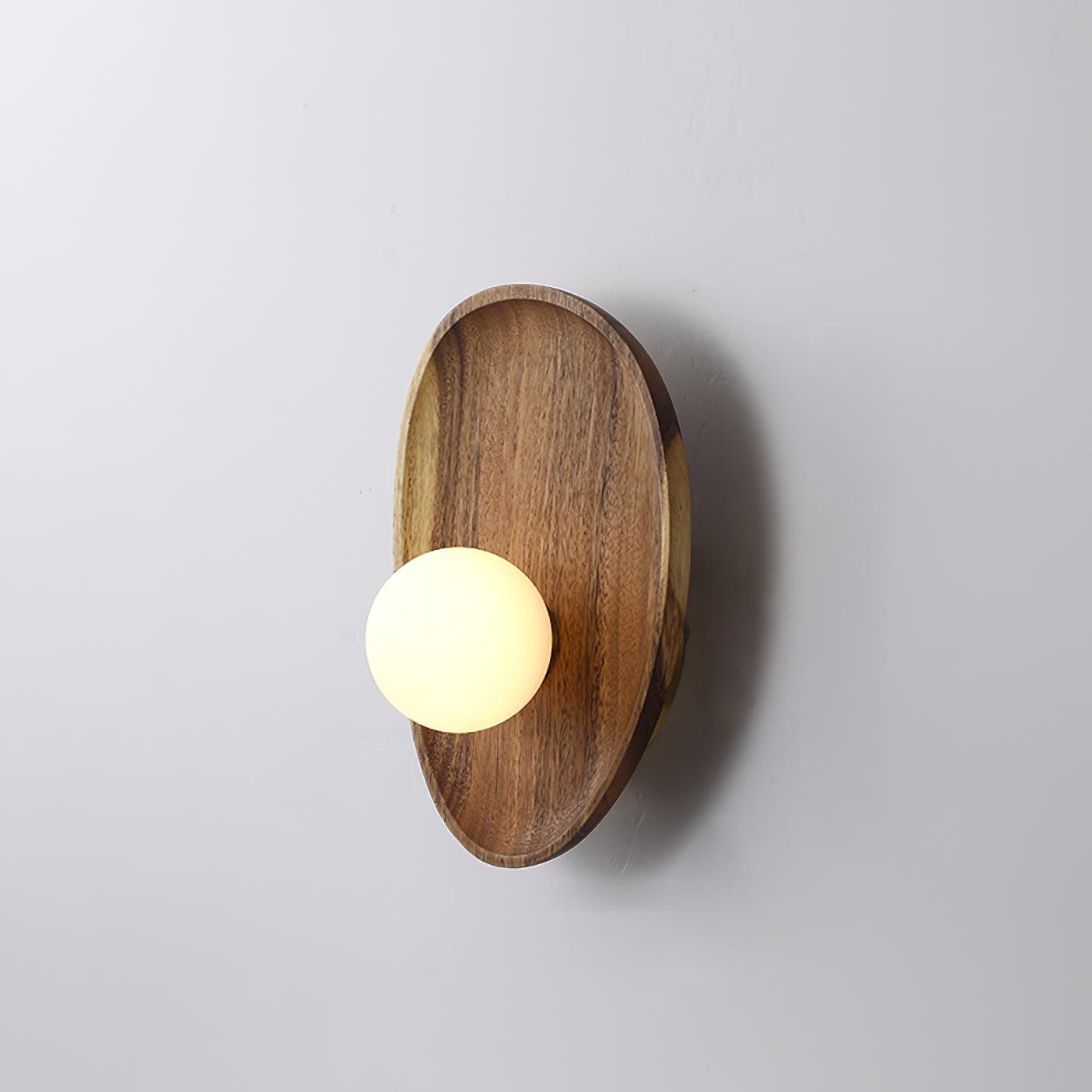 Wall lamp with a shaped walnut-coloured wooden backplate and a white glass globe, wider oval shape, shown on a plain wall.