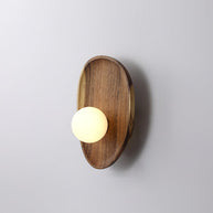 Wall lamp with a shaped walnut-coloured wooden backplate and a white glass globe, wider oval shape, shown on a plain wall.