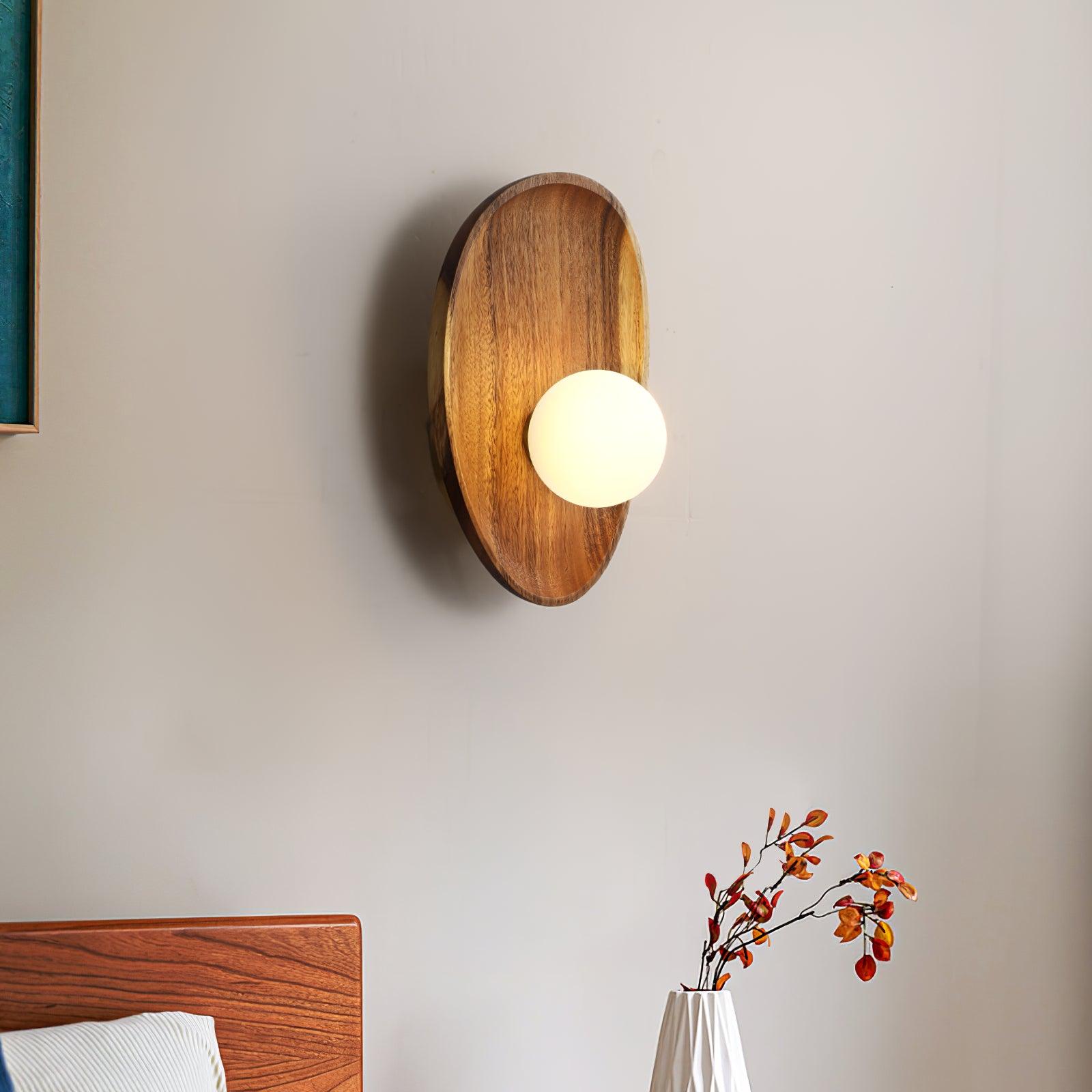 Wall lamp with a shaped walnut-coloured wooden backplate and a white glass globe lit, wider oval shape, seen close on a plain wall.