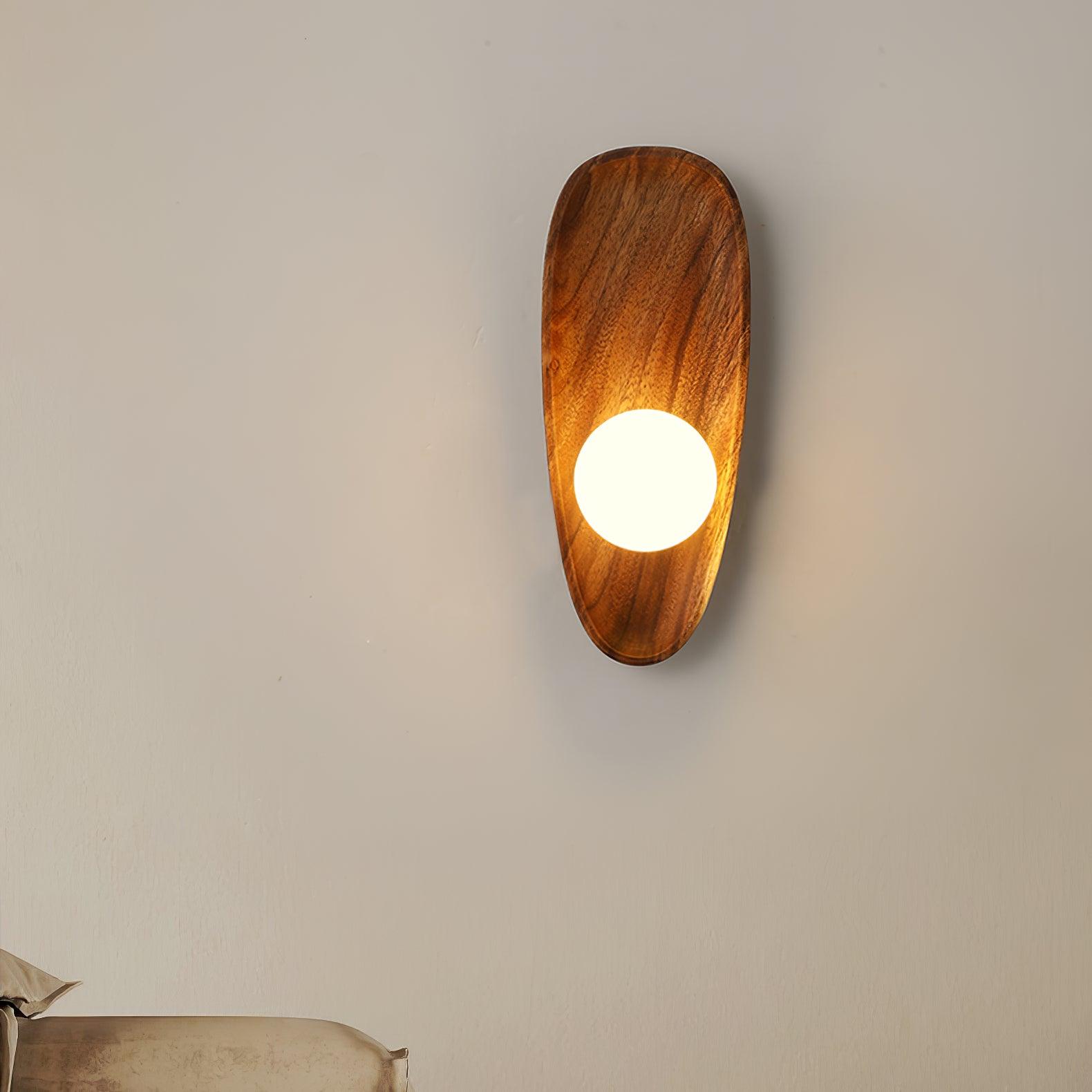 Wall lamp with a shaped walnut-coloured wooden backplate and a white glass globe lit, narrow upright shape, on a plain wall.