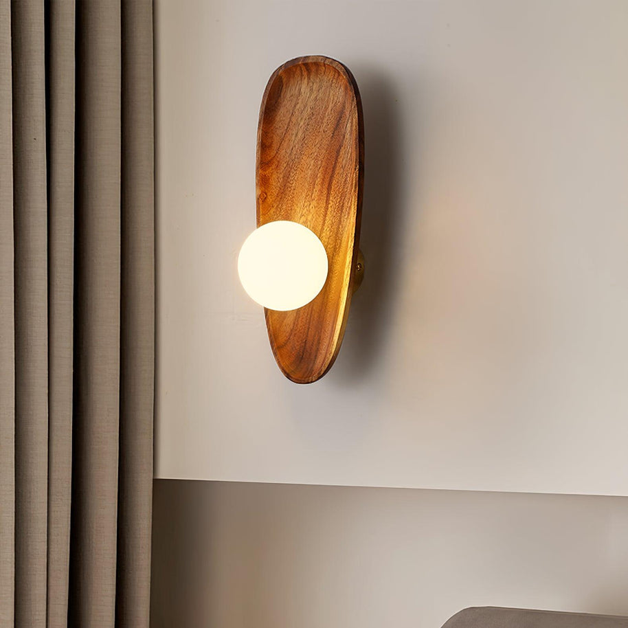 Wall lamp with a shaped walnut-coloured wooden backplate and a white glass globe lit beside a curtain.
