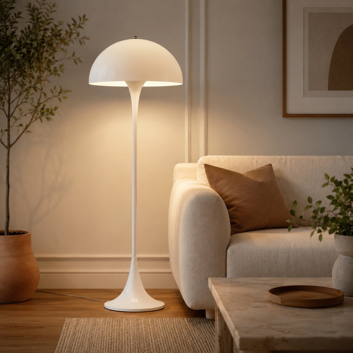 Orla white mushroom dome floor lamp, lit, beside a cream sofa, showing its height next to the seating.