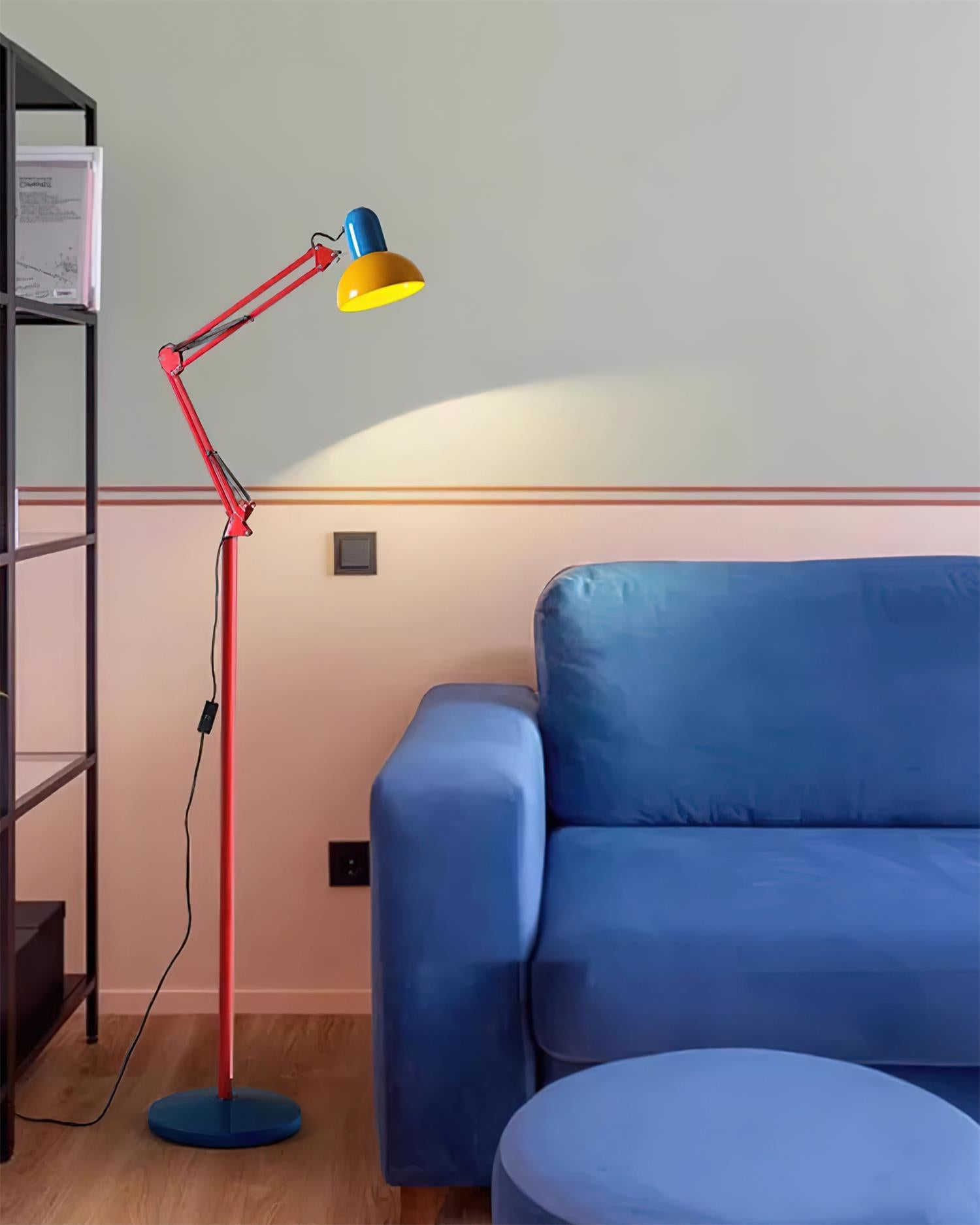 Adjustable floor lamp with a red arm, yellow shade and round blue base lit beside a blue sofa.