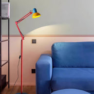 Adjustable floor lamp with a red arm, yellow shade and round blue base lit beside a blue sofa.