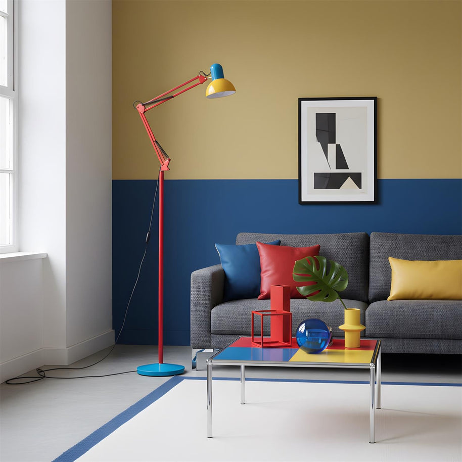 Adjustable floor lamp with a red arm, yellow shade and round blue base in a living room with a grey sofa and a two-tone wall.