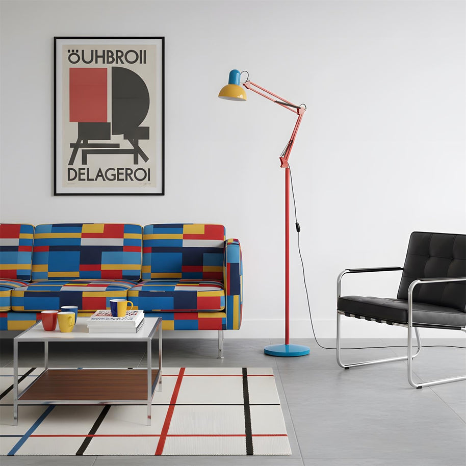 Adjustable floor lamp with a red arm, yellow shade and round blue base in a living room with a colour-block sofa and a poster.