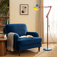 Adjustable floor lamp with a red arm, yellow shade and round blue base beside a blue armchair holding an open book.