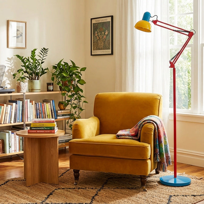 Adjustable floor lamp with a red arm, yellow shade and round blue base beside a mustard armchair at a sunlit window.