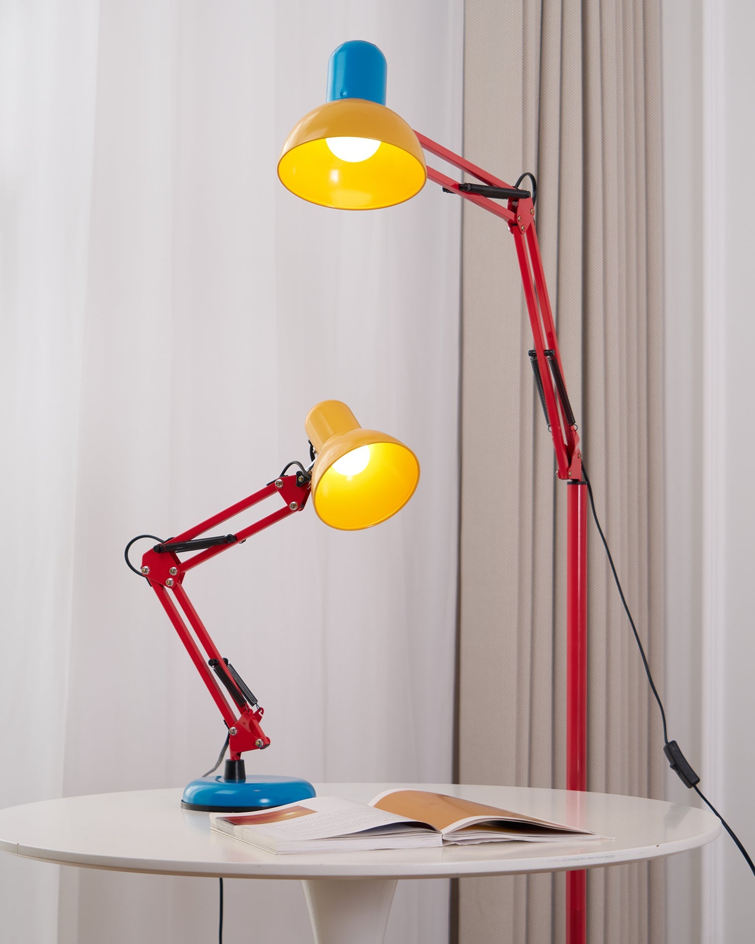 Tall floor lamp with a red adjustable arm, yellow shade and blue top, shown lit beside a matching table lamp.