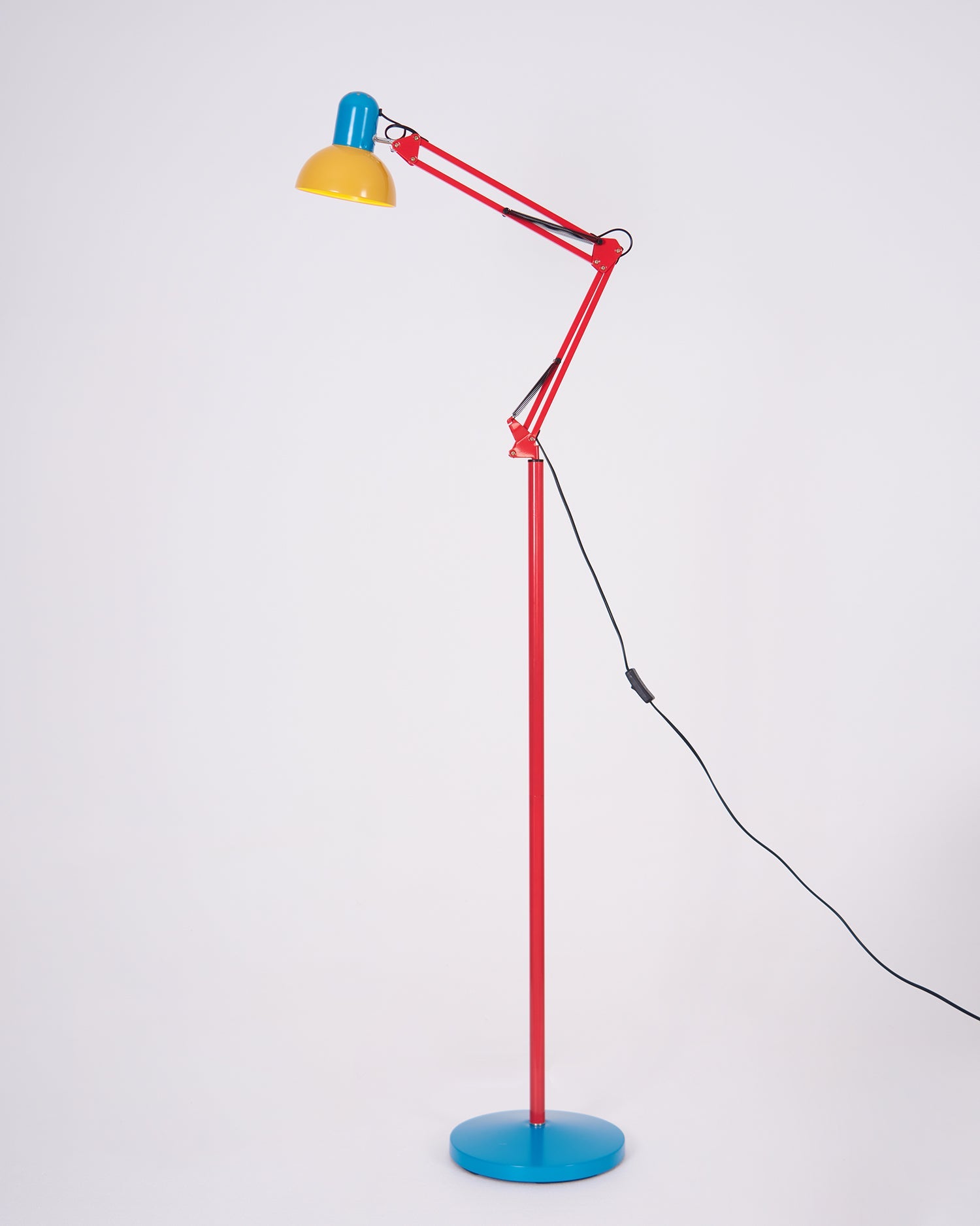 Adjustable floor lamp with a red arm, yellow shade and round blue base with the arm angled forward, on a plain background.