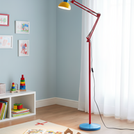 Adjustable floor lamp with a red arm, yellow shade and round blue base in a child's play corner beside a low shelf and toys.