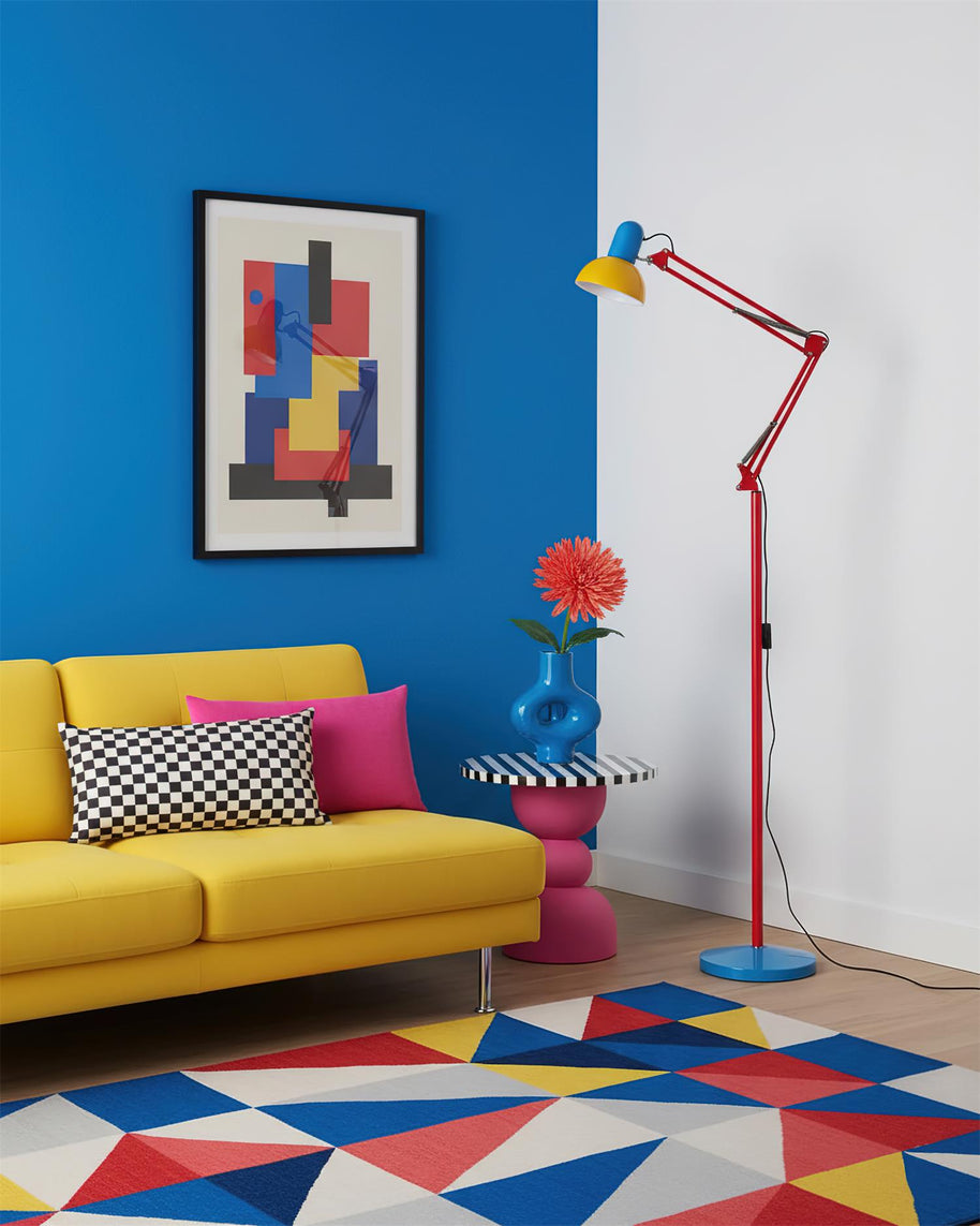 Adjustable floor lamp with a red arm, yellow shade and round blue base in a living room with a yellow sofa against a blue wall.