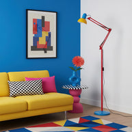 Adjustable floor lamp with a red arm, yellow shade and round blue base in a living room with a yellow sofa against a blue wall.