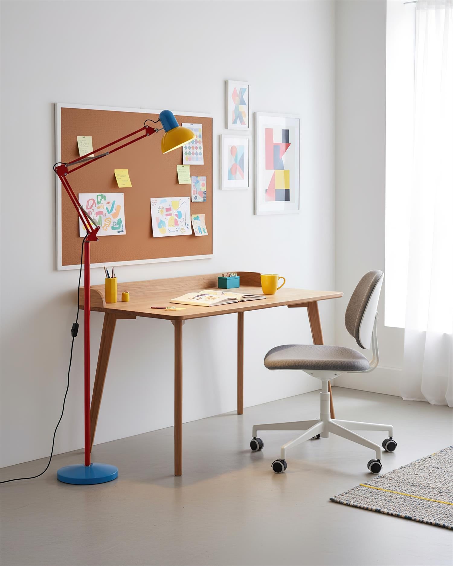 Adjustable floor lamp with a red arm, yellow shade and round blue base beside a wooden desk and a pinboard.