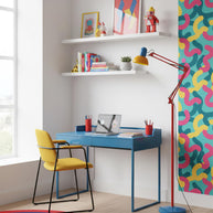 Adjustable floor lamp with a red arm, yellow shade and round blue base in a home office with a blue desk and a yellow chair.