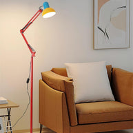 Adjustable floor lamp with a red arm, yellow shade and round blue base beside a tan armchair in a living room.