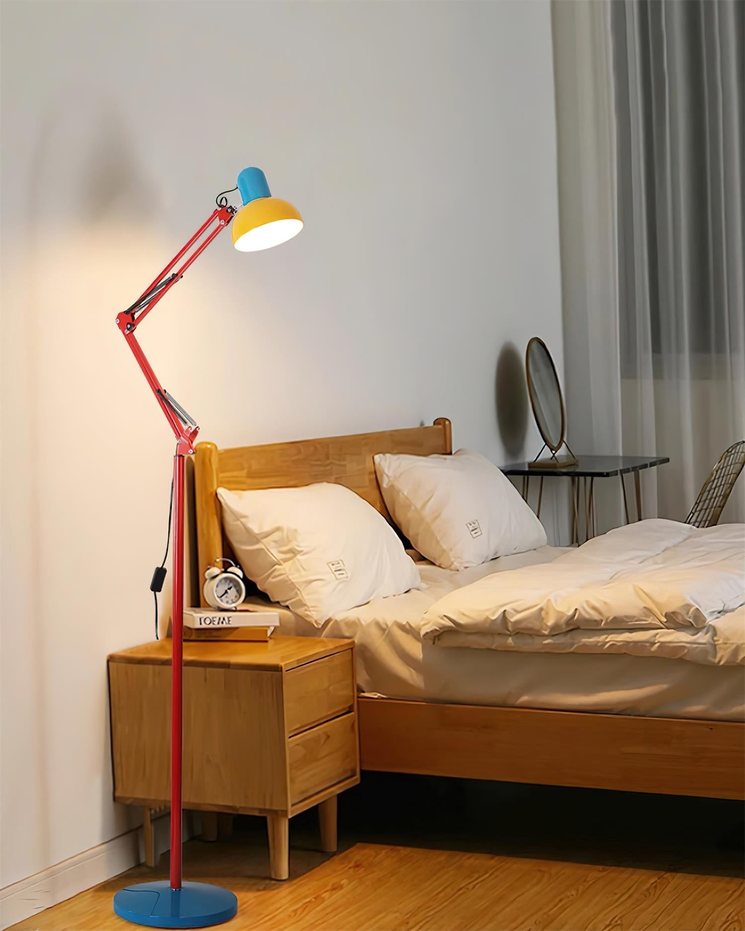 Adjustable floor lamp with a red arm, yellow shade and round blue base lit beside a wooden bed.