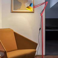 Adjustable floor lamp with a red arm, yellow shade and round blue base lit beside a mustard chair near a doorway.