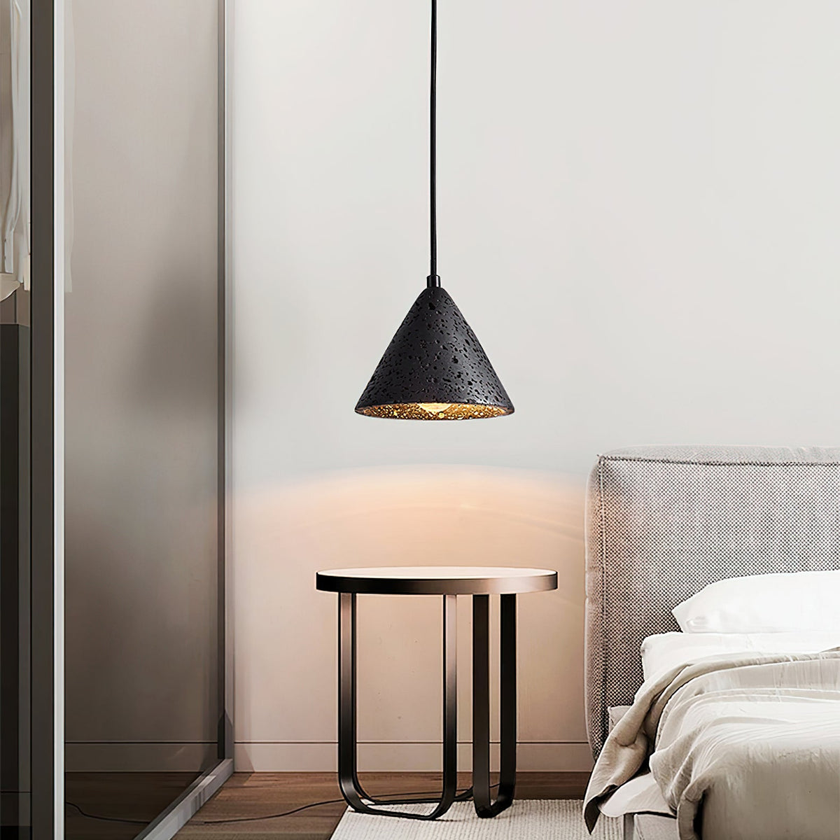 Halovyn Pendant Light in black travertine, cone shade lit above a round side table beside a bed