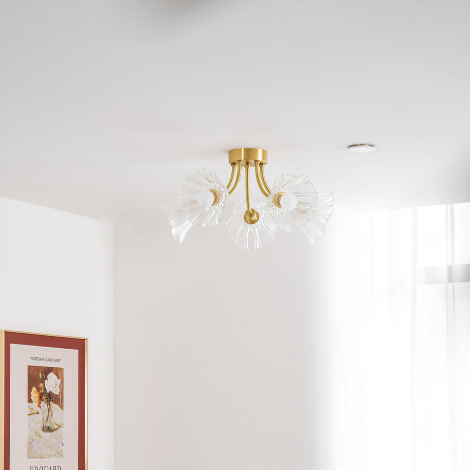 Flush-mount ceiling lamp with curved brass arms holding clear ribbed flower-shaped glass shades on a ceiling seen from below, beside a window.
