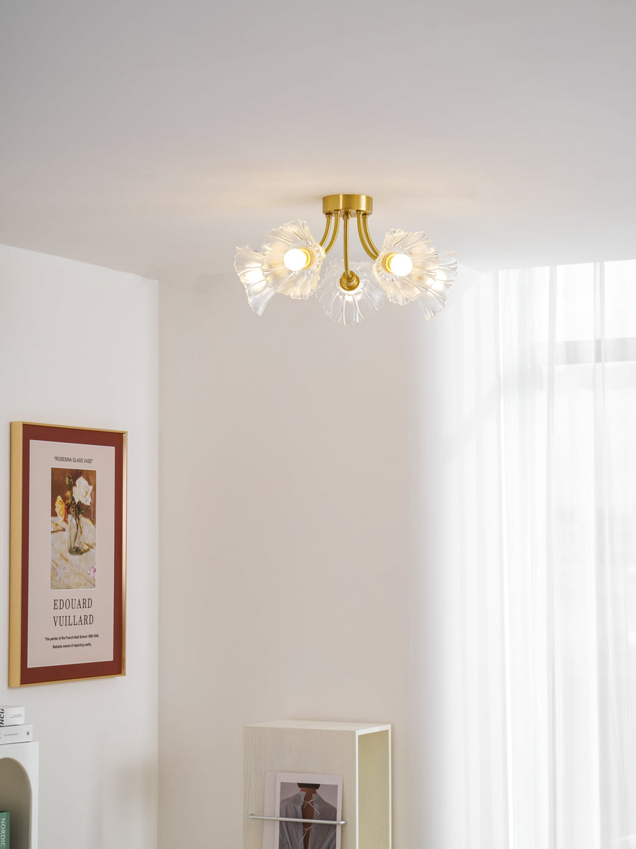 Flush-mount ceiling lamp with curved brass arms holding clear ribbed flower-shaped glass shades lit on a ceiling in a bright corner.