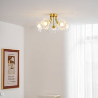 Flush-mount ceiling lamp with curved brass arms holding clear ribbed flower-shaped glass shades lit on a ceiling in a bright corner.