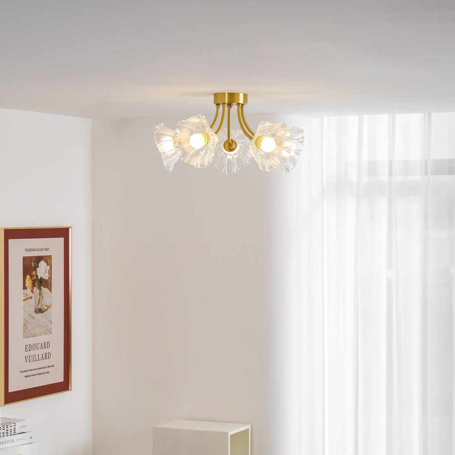 Flush-mount ceiling lamp with curved brass arms holding clear ribbed flower-shaped glass shades lit on a ceiling beside a window.