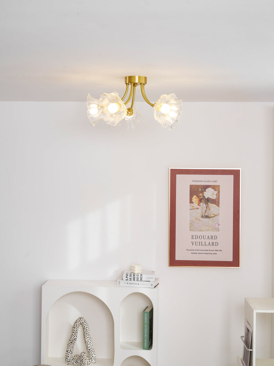 Flush-mount ceiling lamp with curved brass arms holding clear ribbed flower-shaped glass shades lit on a ceiling above an alcove shelf.