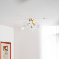 Flush-mount ceiling lamp with curved brass arms holding clear ribbed flower-shaped glass shades on a ceiling seen from below, beside a window.