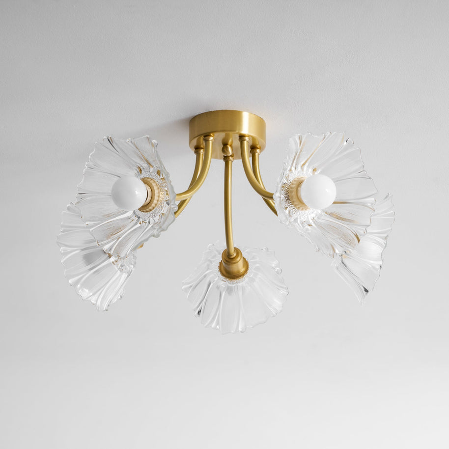 Flush-mount ceiling lamp with curved brass arms holding clear ribbed flower-shaped glass shades, lit, seen from below and to one side.