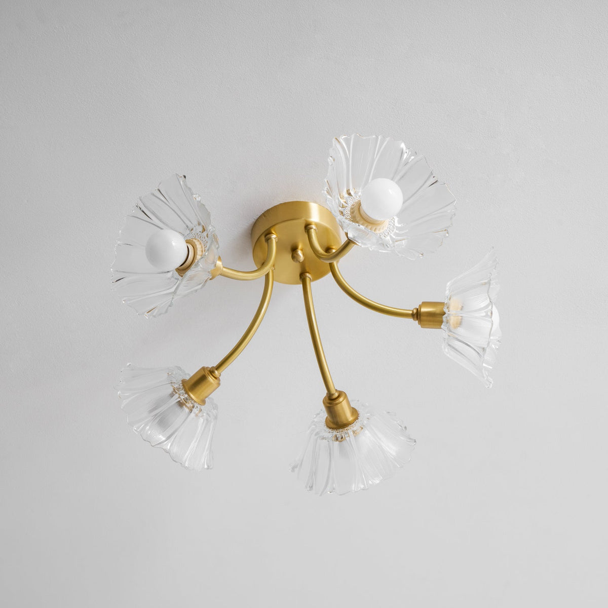 Flush-mount ceiling lamp with curved brass arms holding clear ribbed flower-shaped glass shades, unlit, seen from below.