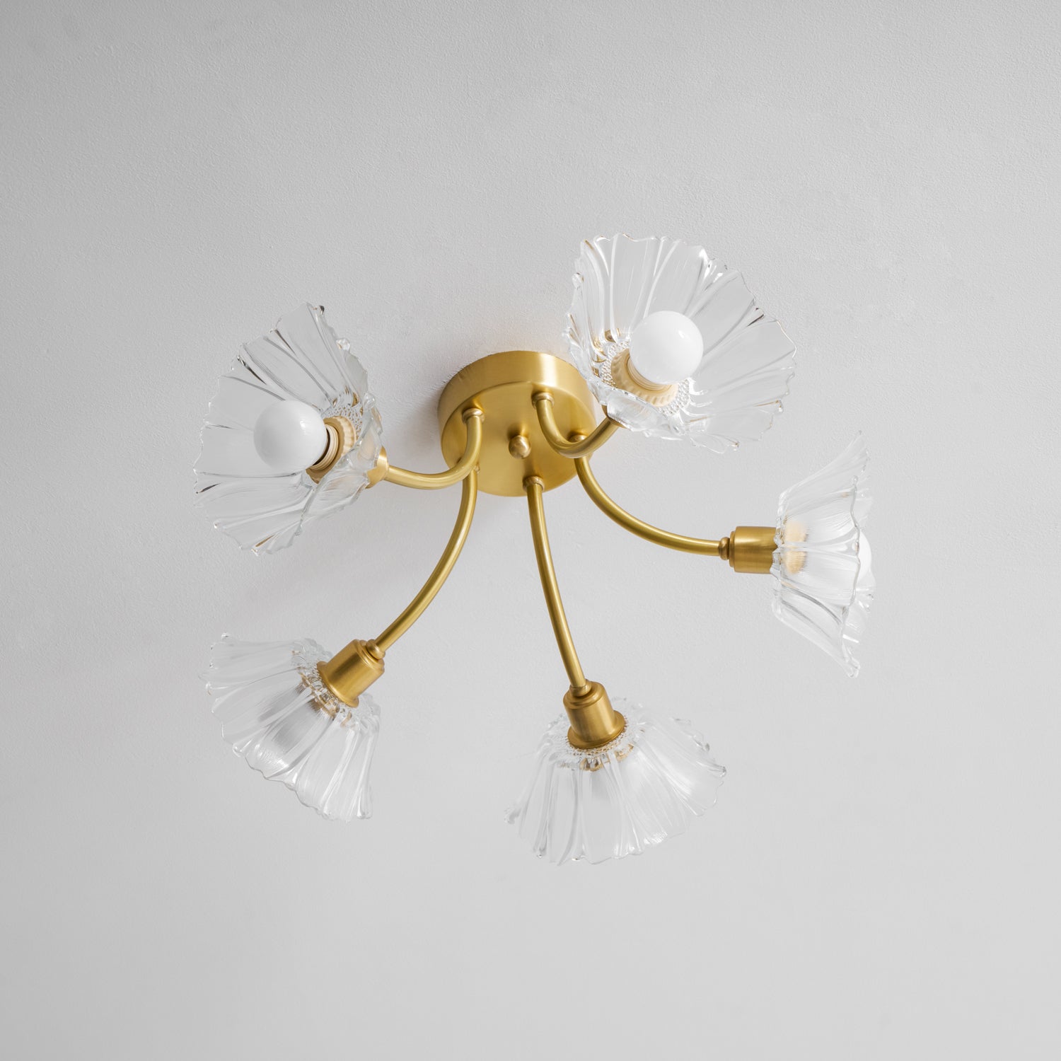 Flush-mount ceiling lamp with curved brass arms holding clear ribbed flower-shaped glass shades, unlit, seen from below.